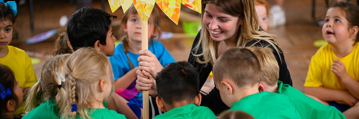 A teacher holds a brightly coloured sunflower at the centre of a group of children in green t-shirts