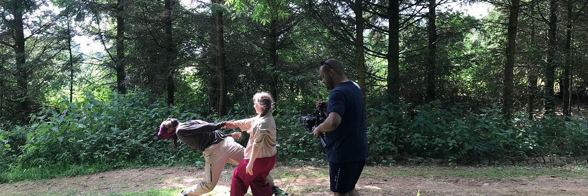 Two dancers perform on a wooded path in Dorset, near the site of a buried Iron Age settlement. They are filmed by a single film director with a camera, Dan Martin.
